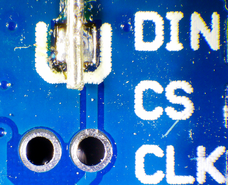 Magnified photo of a MAX7219 display module with two open holes for a capacitor next to the CS and CLK pins.